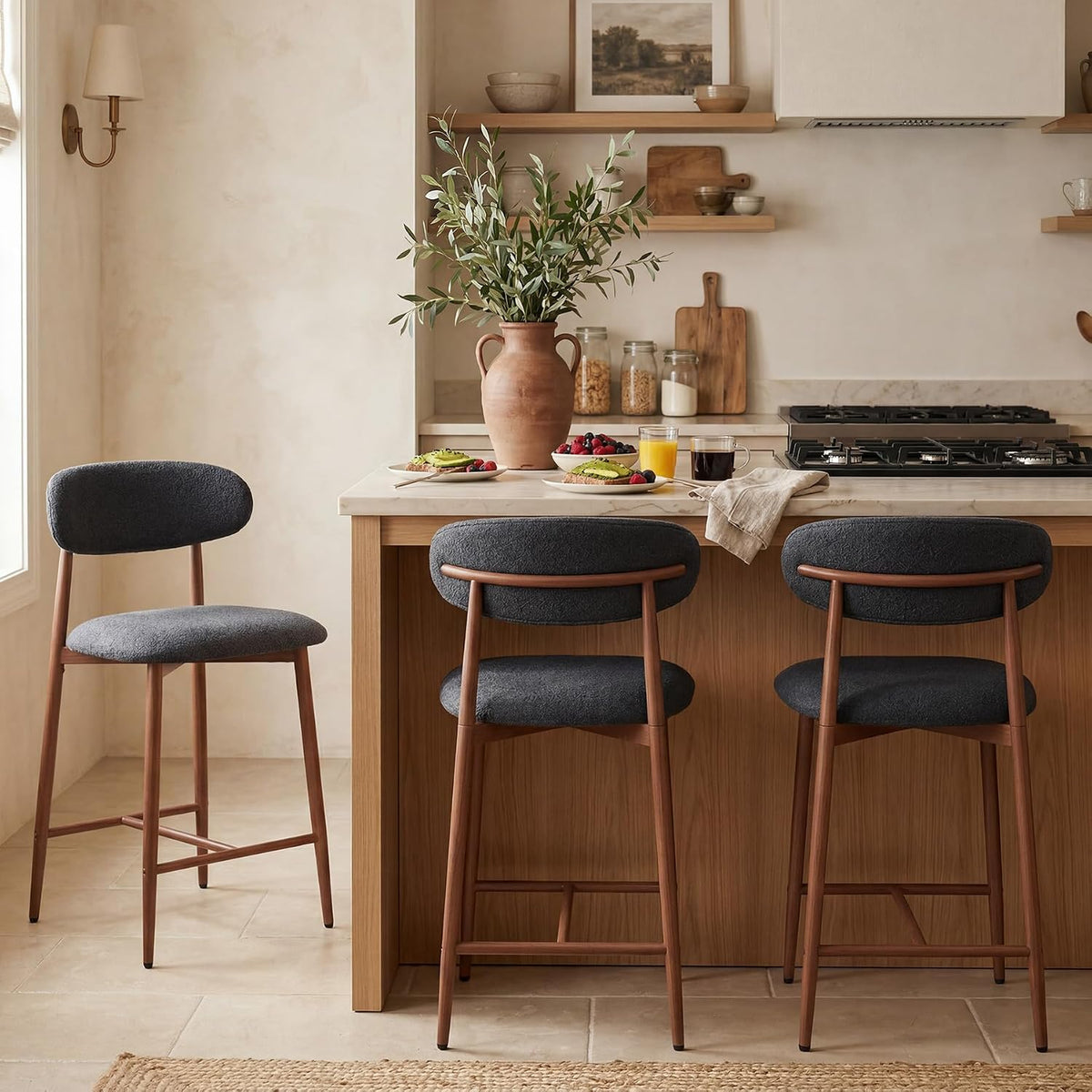 Kitchen island with three dark gray upholstered counter-height stools with warm brown legs.