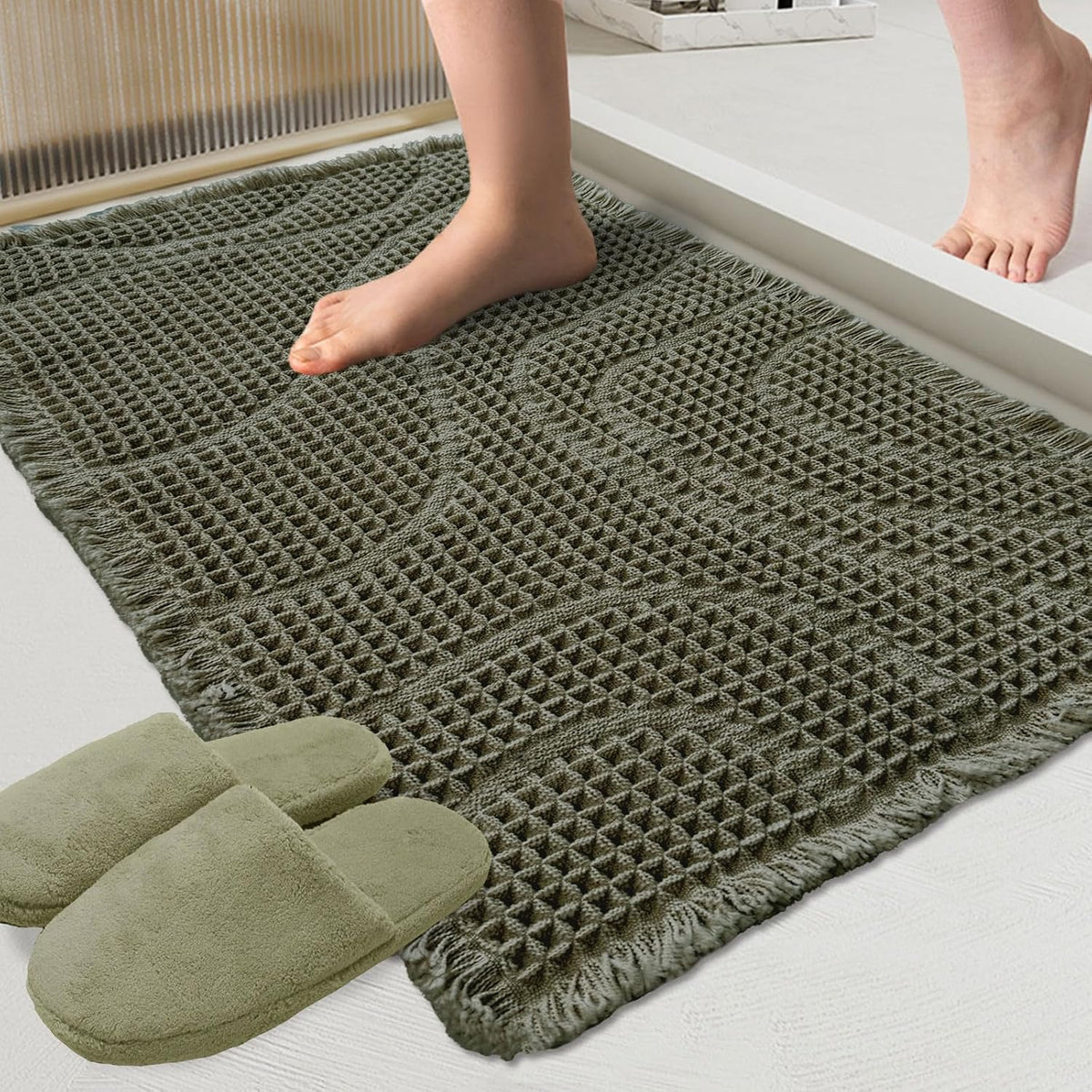 Close-up of olive-green woven mat texture and fringe with a bare foot stepping onto it and slippers nearby