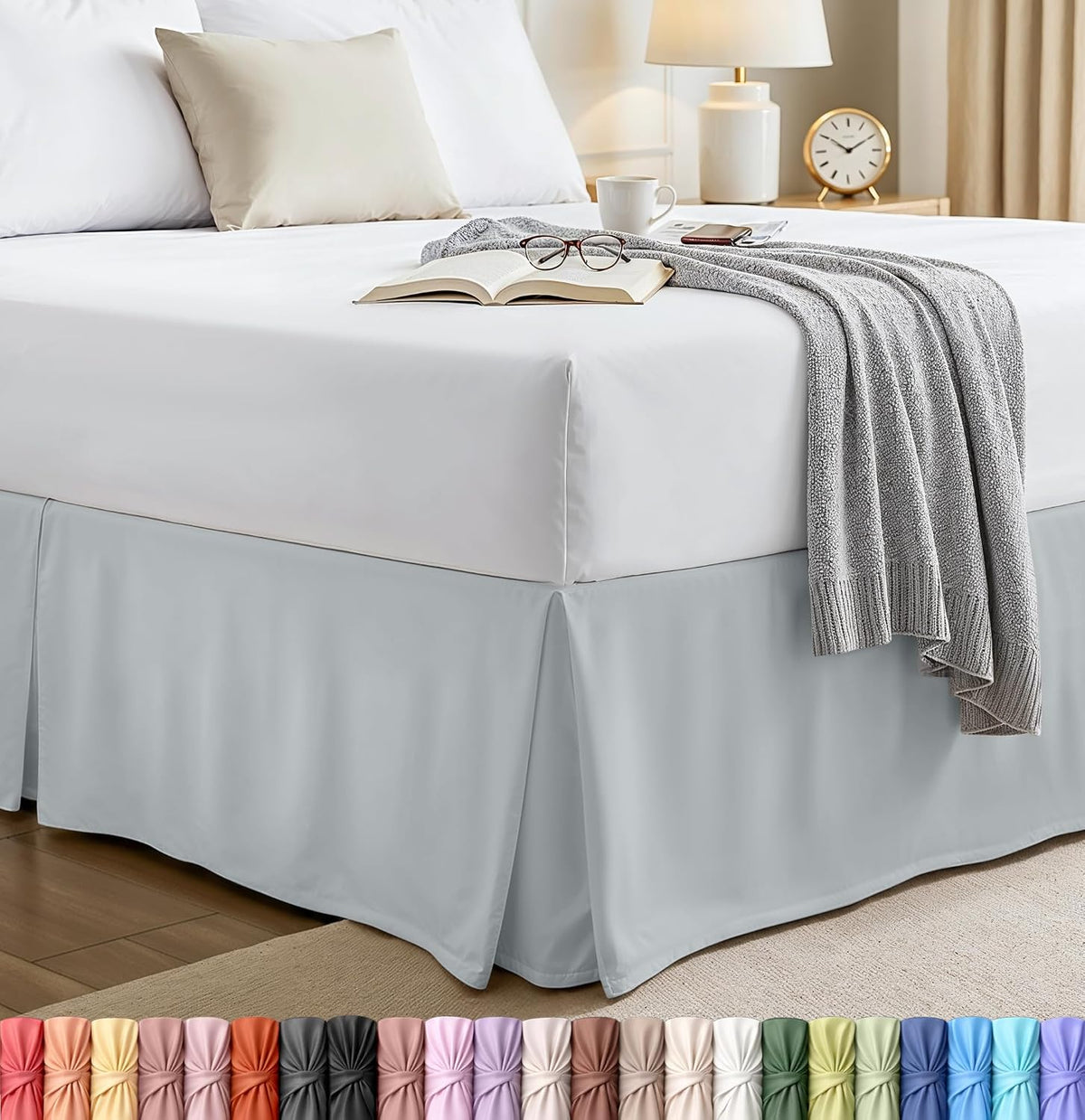 Bed corner with a light gray pleated bed skirt, white sheets and a gray throw draped over the mattress