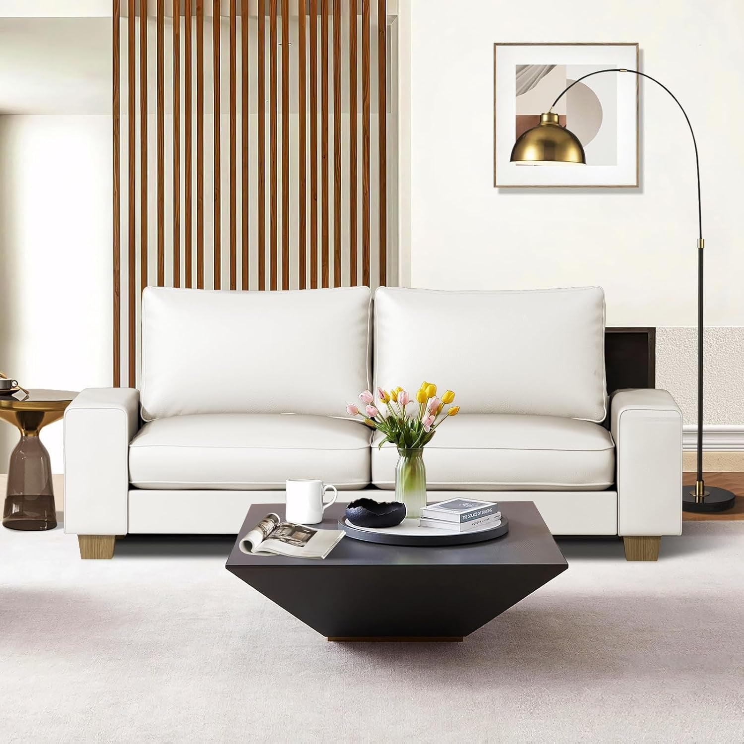 Front view of an off-white faux-leather loveseat staged with a dark geometric coffee table and arched floor lamp
