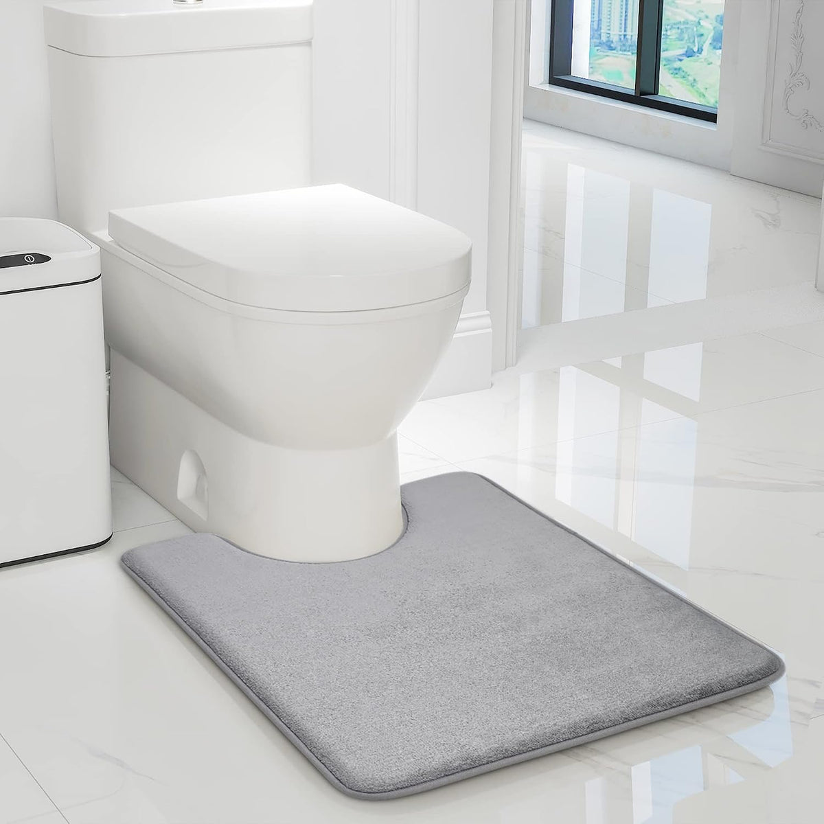 Toilet beside a gray contoured memory-foam bath rug on glossy white tile floor.