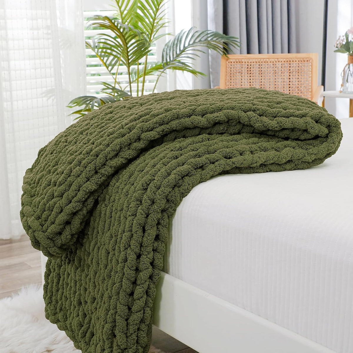 Olive-green chunky knit throw folded and draped over the side of a white bed.