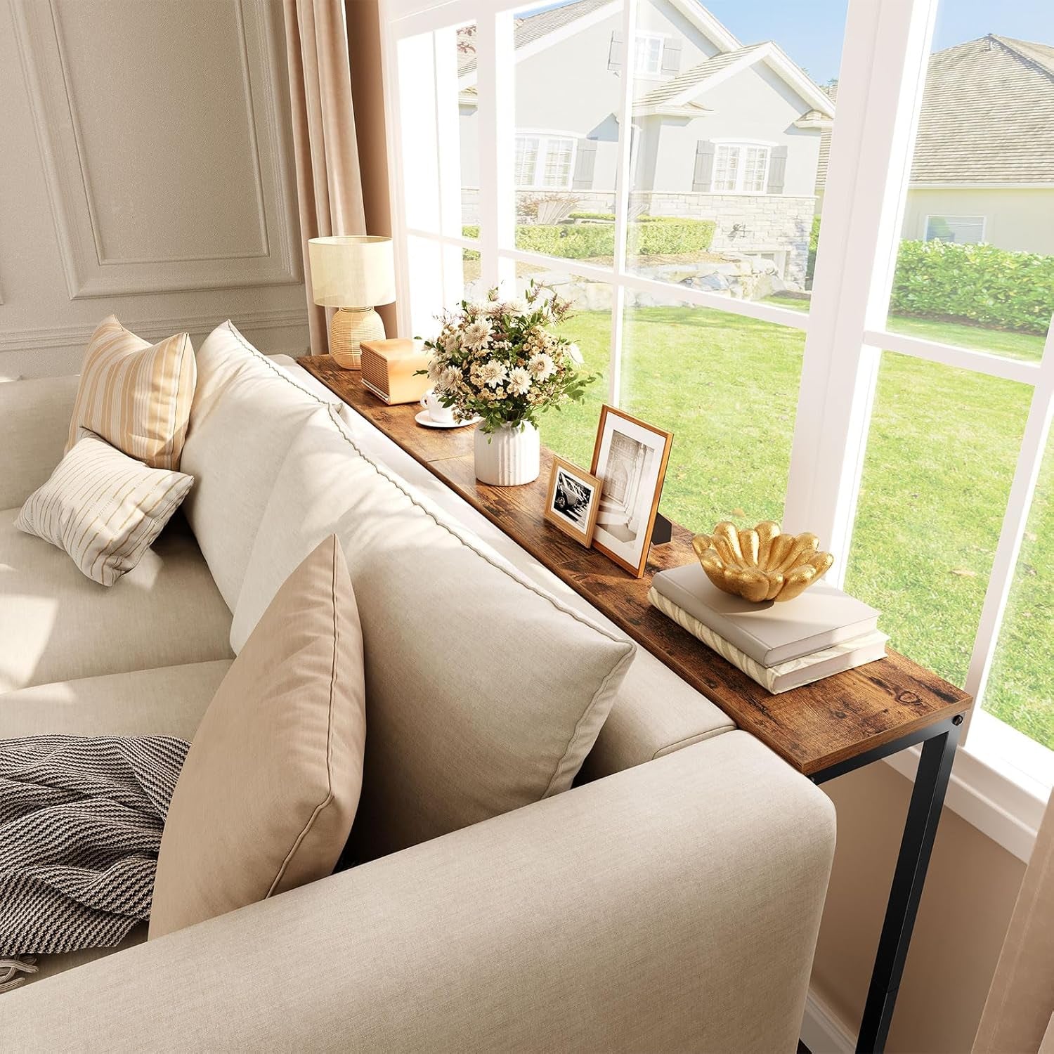 Console table placed behind a sofa holding decorative vases and photo frames along a sunny window
