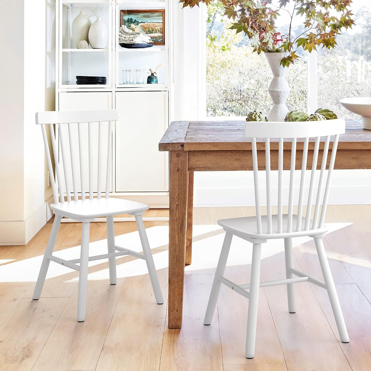 Two white spindle-back wooden dining chairs placed beside a wooden table in a sunlit dining area