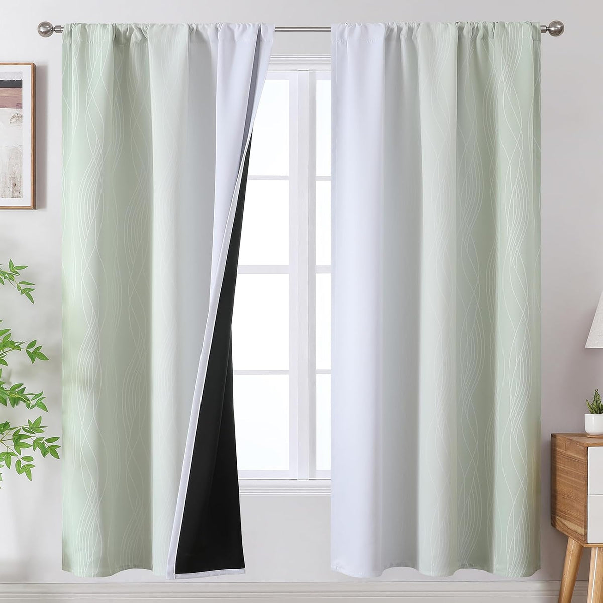 Window with light mint-green curtains hung on a rod, one panel pulled back to expose white interior and black blackout layer.