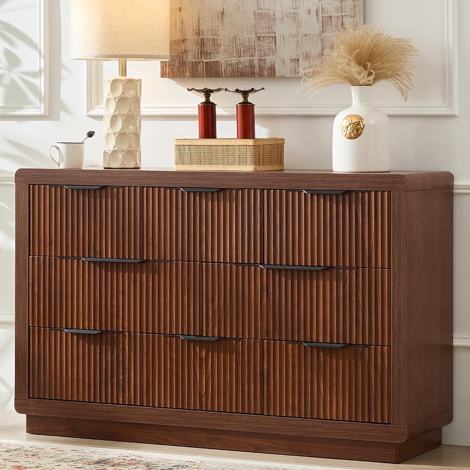 Medium brown wide ribbed dresser with six drawers, decorative vase and lamp arranged on the top.
