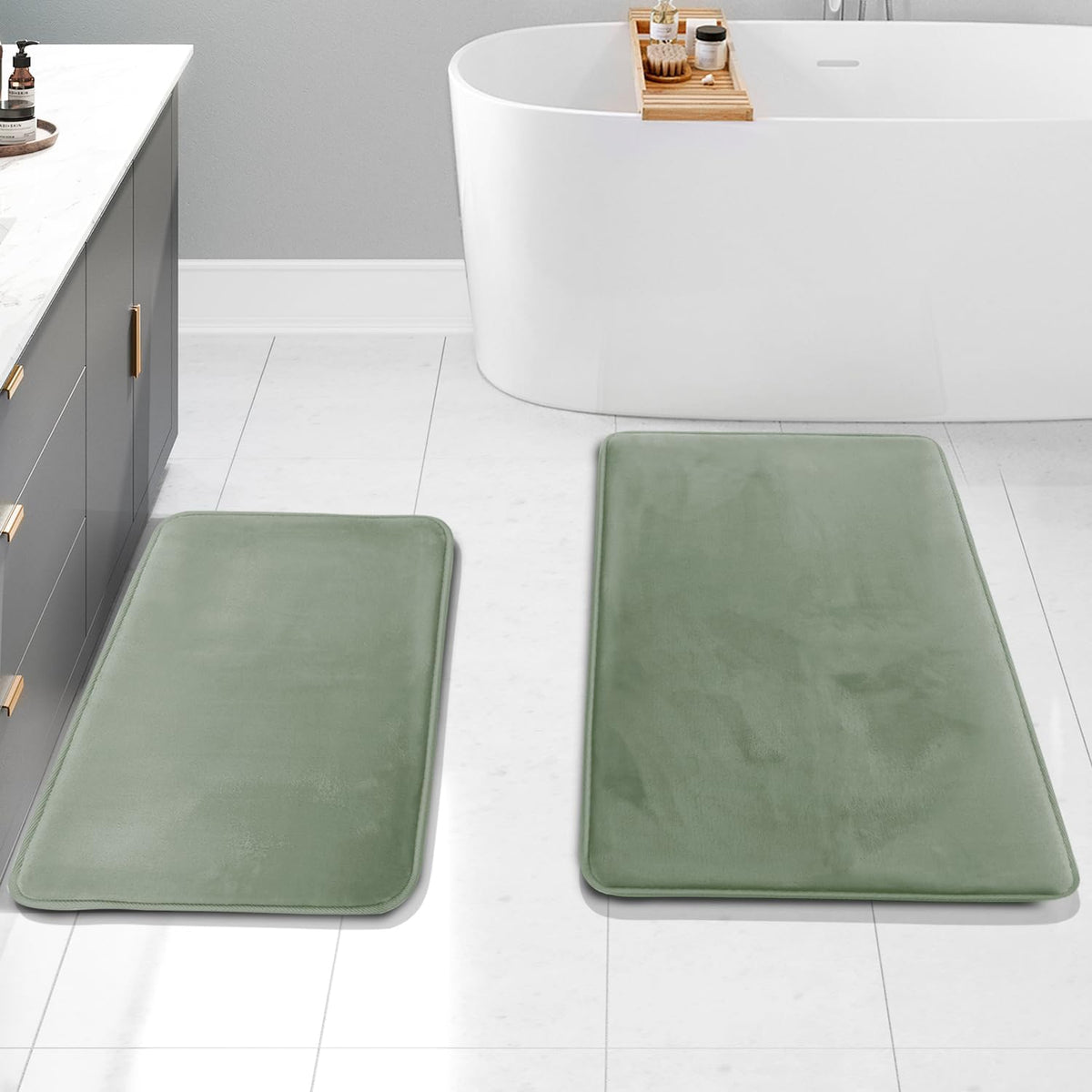 Overhead view of two sage-green rectangular mats placed on the floor beside a freestanding bathtub.