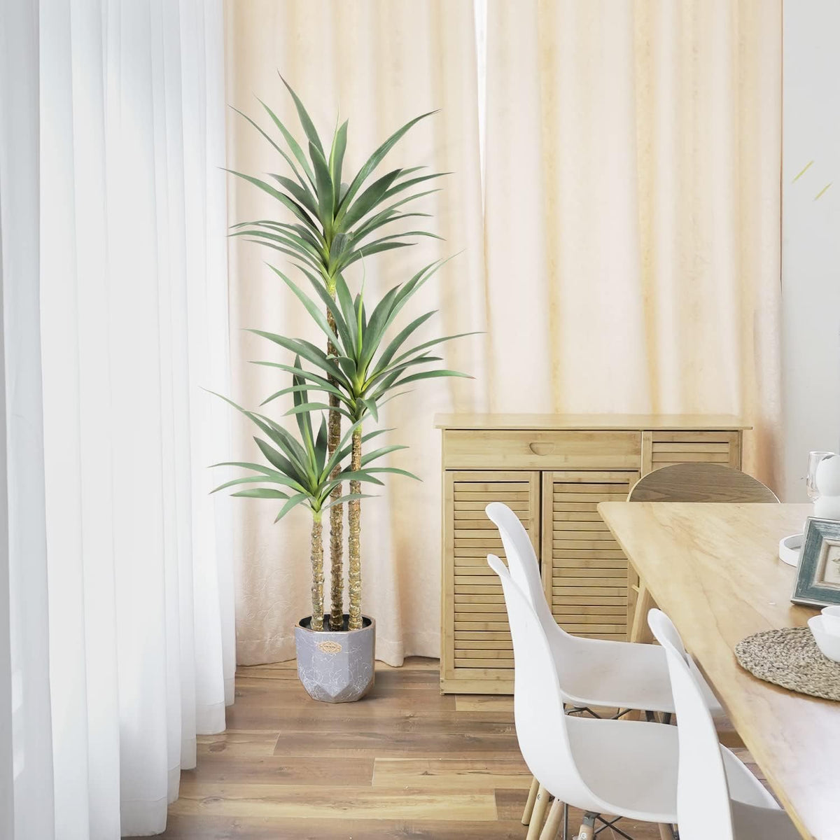 Potted artificial agave tree near a dining table and curtains in a light-filled dining area