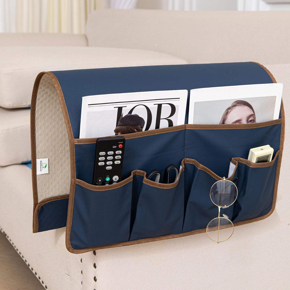 Navy faux-leather armrest caddy hung over a light sofa arm with magazines and remotes in pockets.