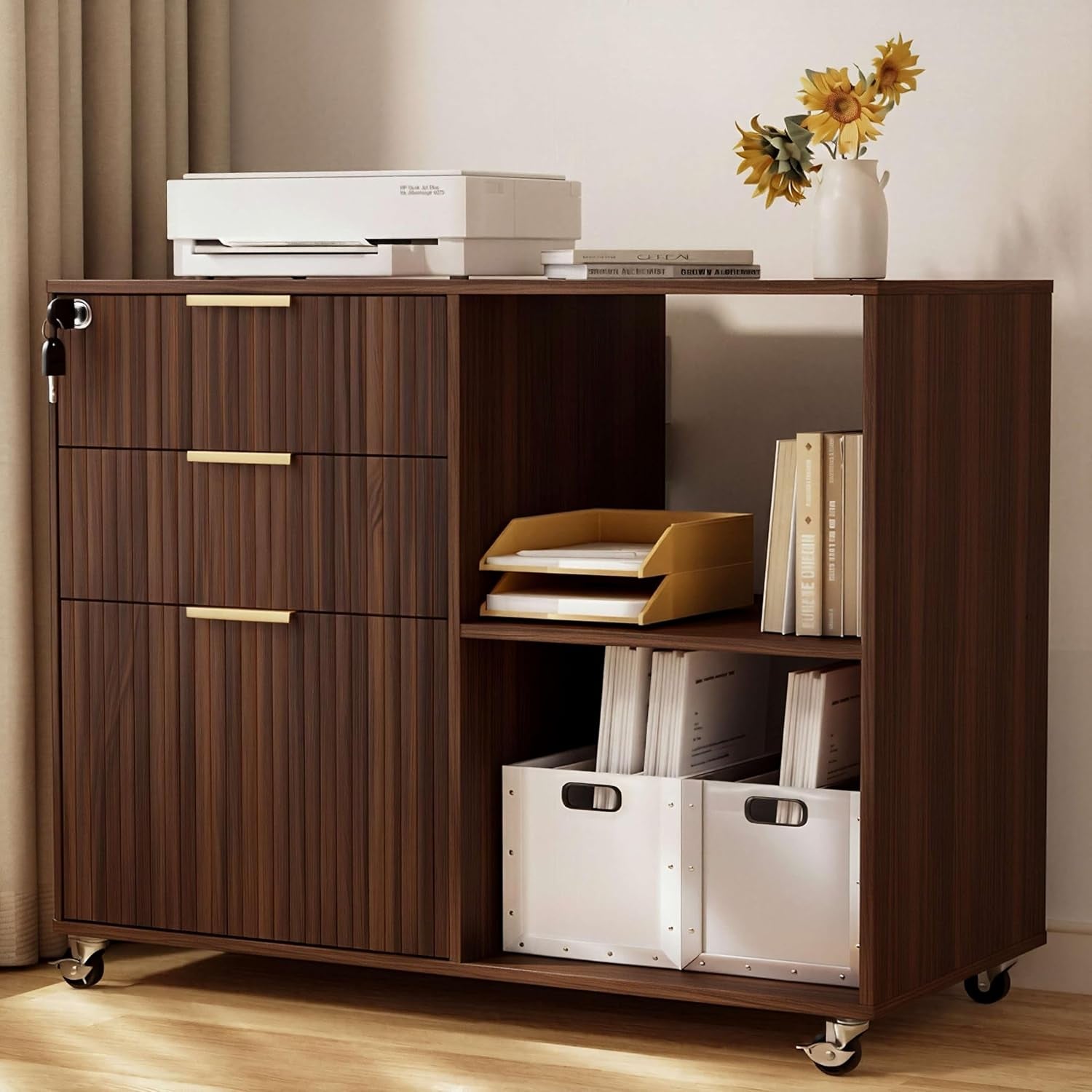 Three-quarter view of a dark wood three-drawer mobile cabinet with open cubbies, paper trays, white storage boxes and a vase.