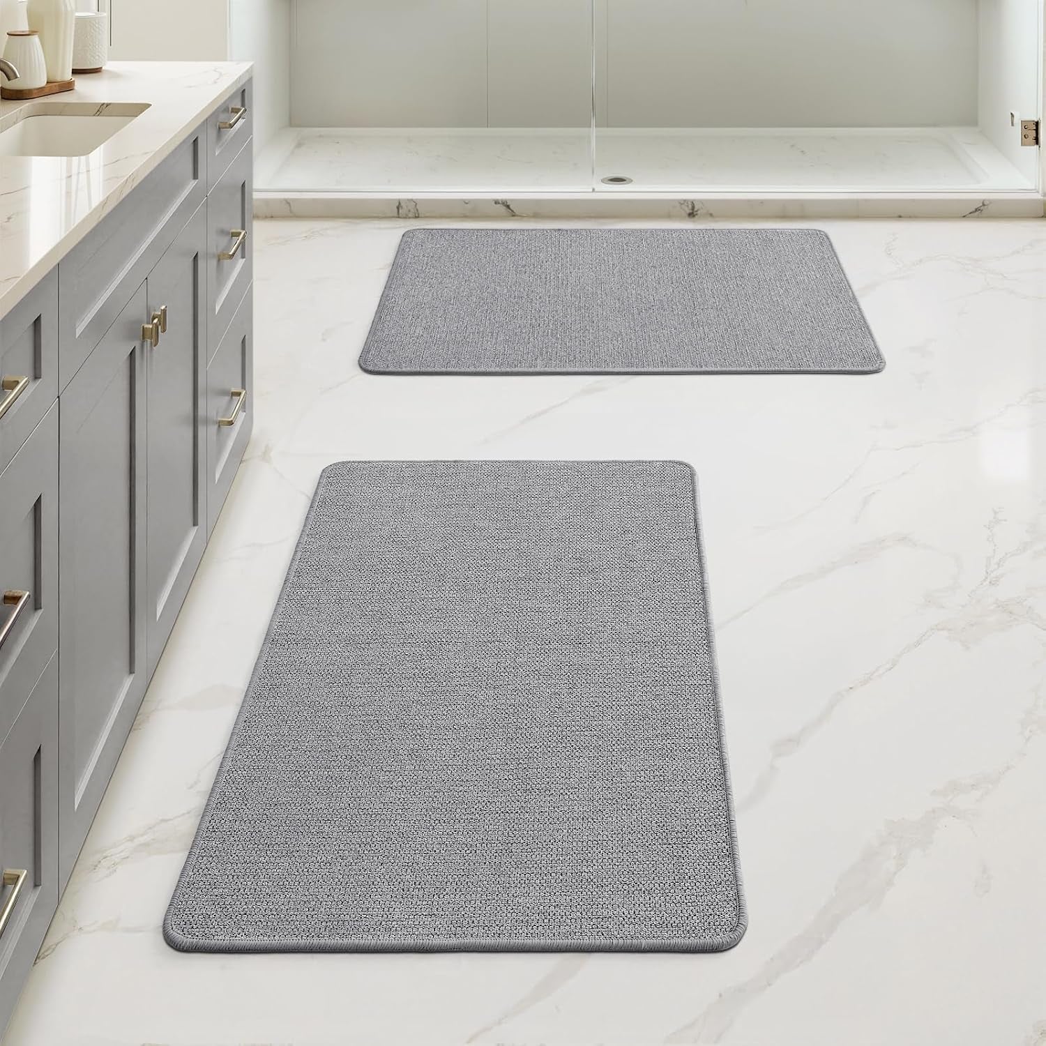 Bathroom floor with two rectangular light-gray bath rugs placed near sink and shower