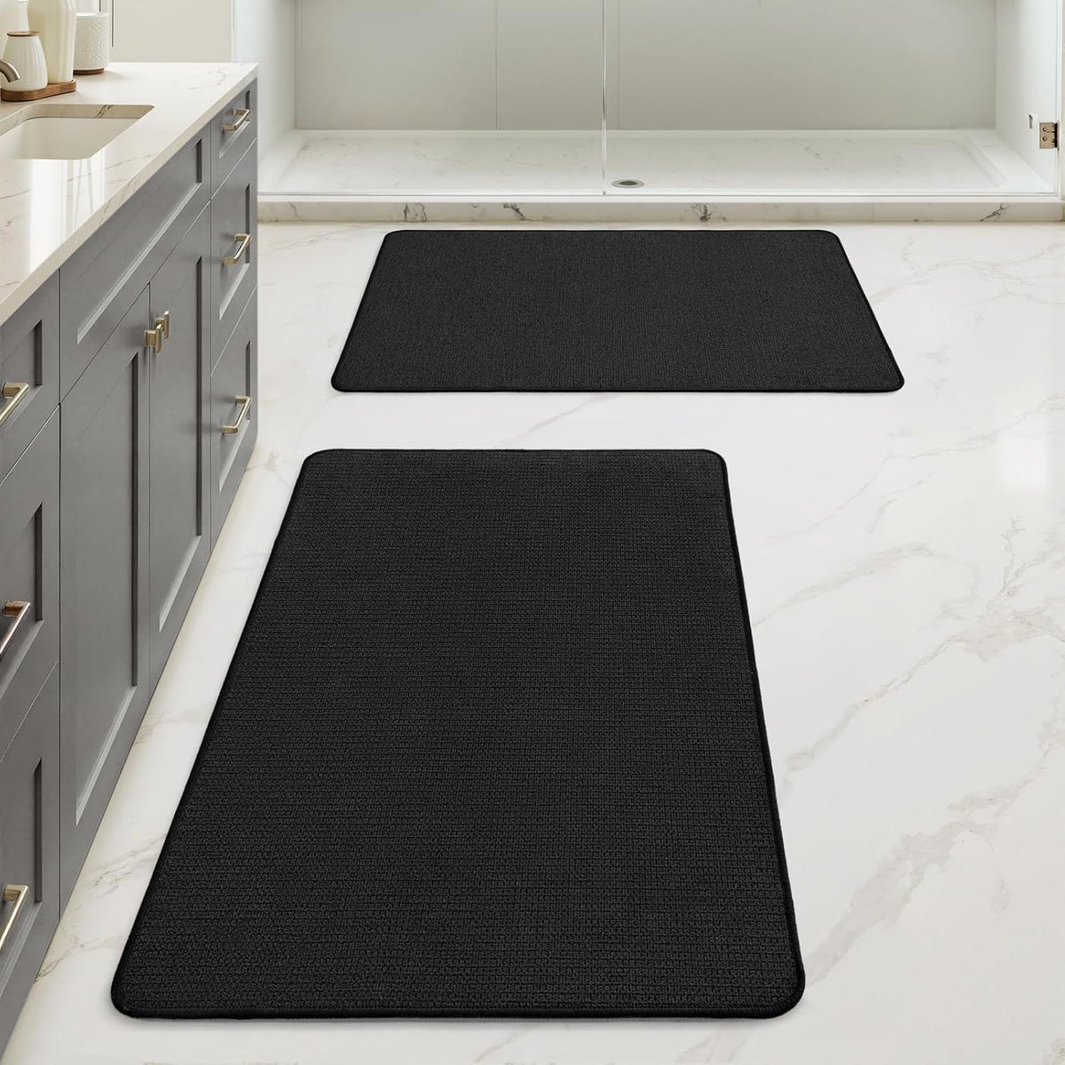 Bathroom floor with two rectangular black rugs aligned along the vanity and shower.