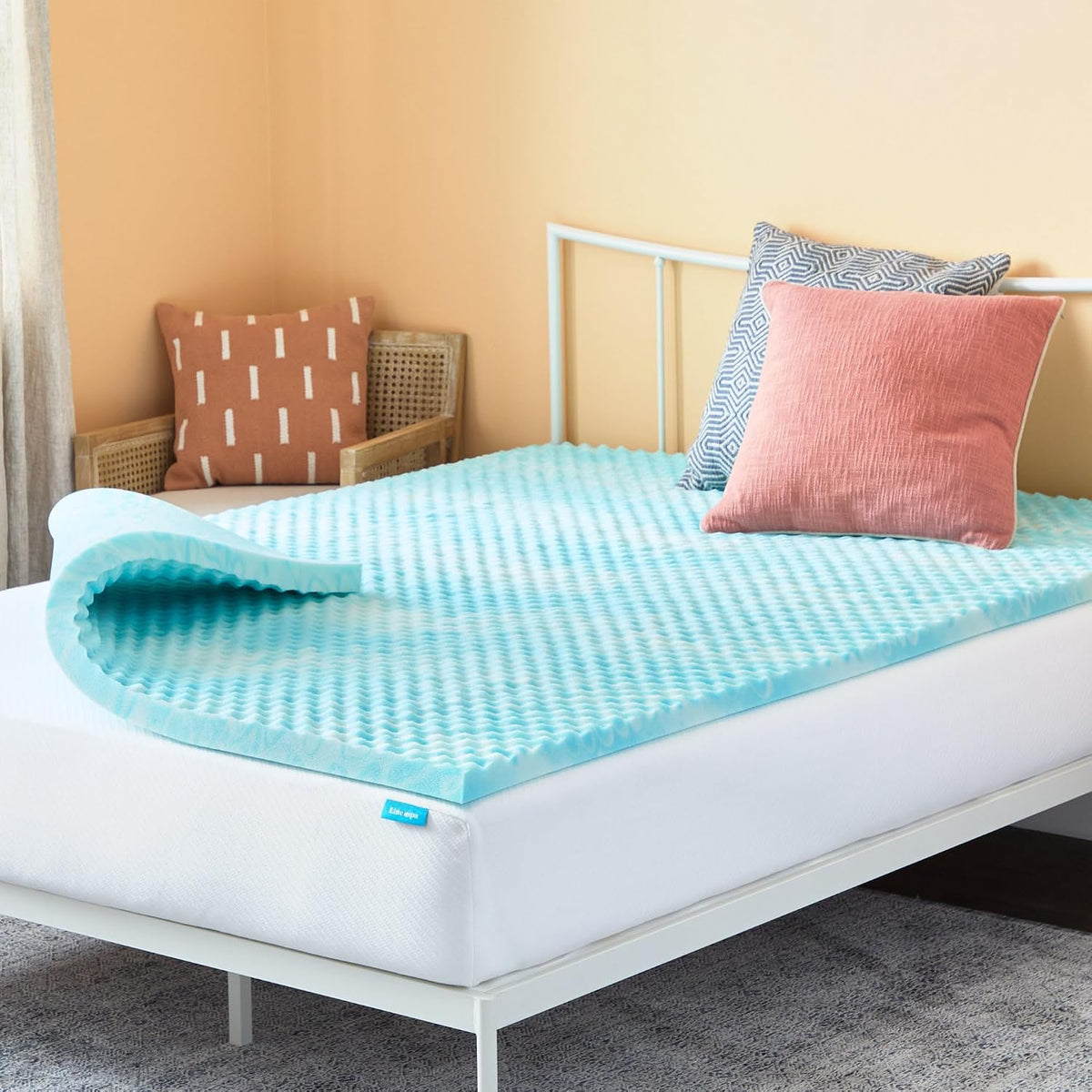 Top view showing egg-crate textured light blue foam topper curled at one end on a bed