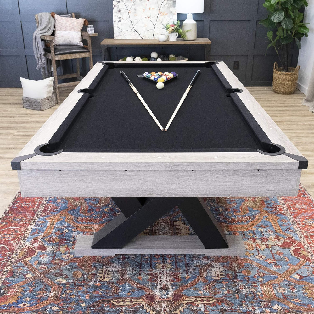 Front view of the table showing X-shaped black legs, light wood frame and black pockets on a patterned rug