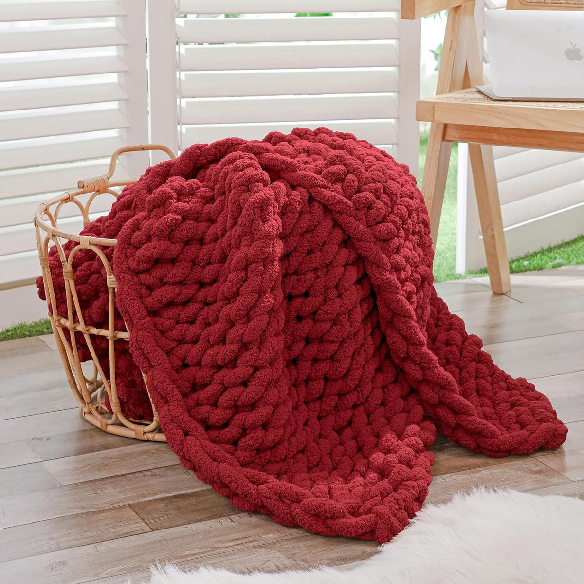 Deep red chunky chenille throw draped loosely inside a round woven basket on a wood floor.