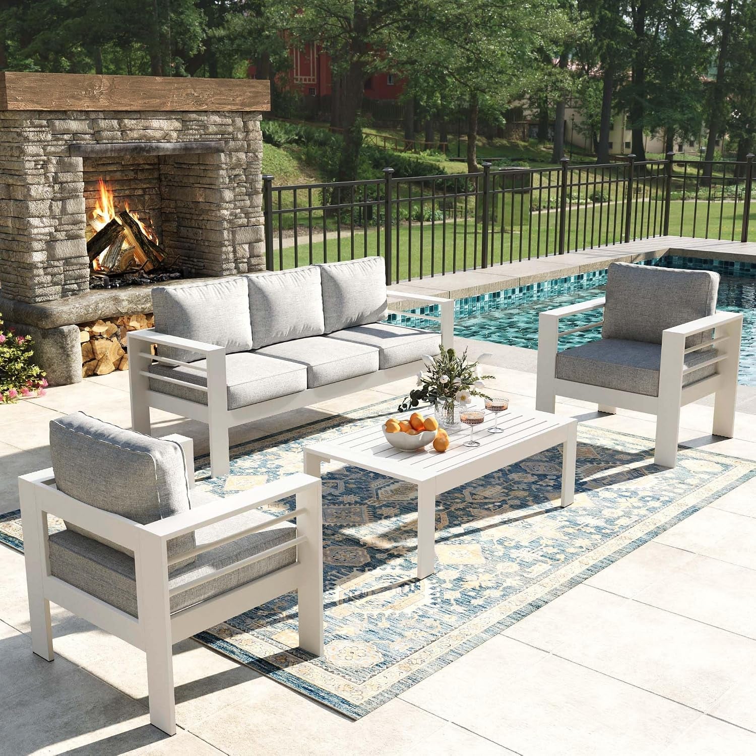 White-framed patio conversation set with gray cushions arranged on a patterned rug by a pool.