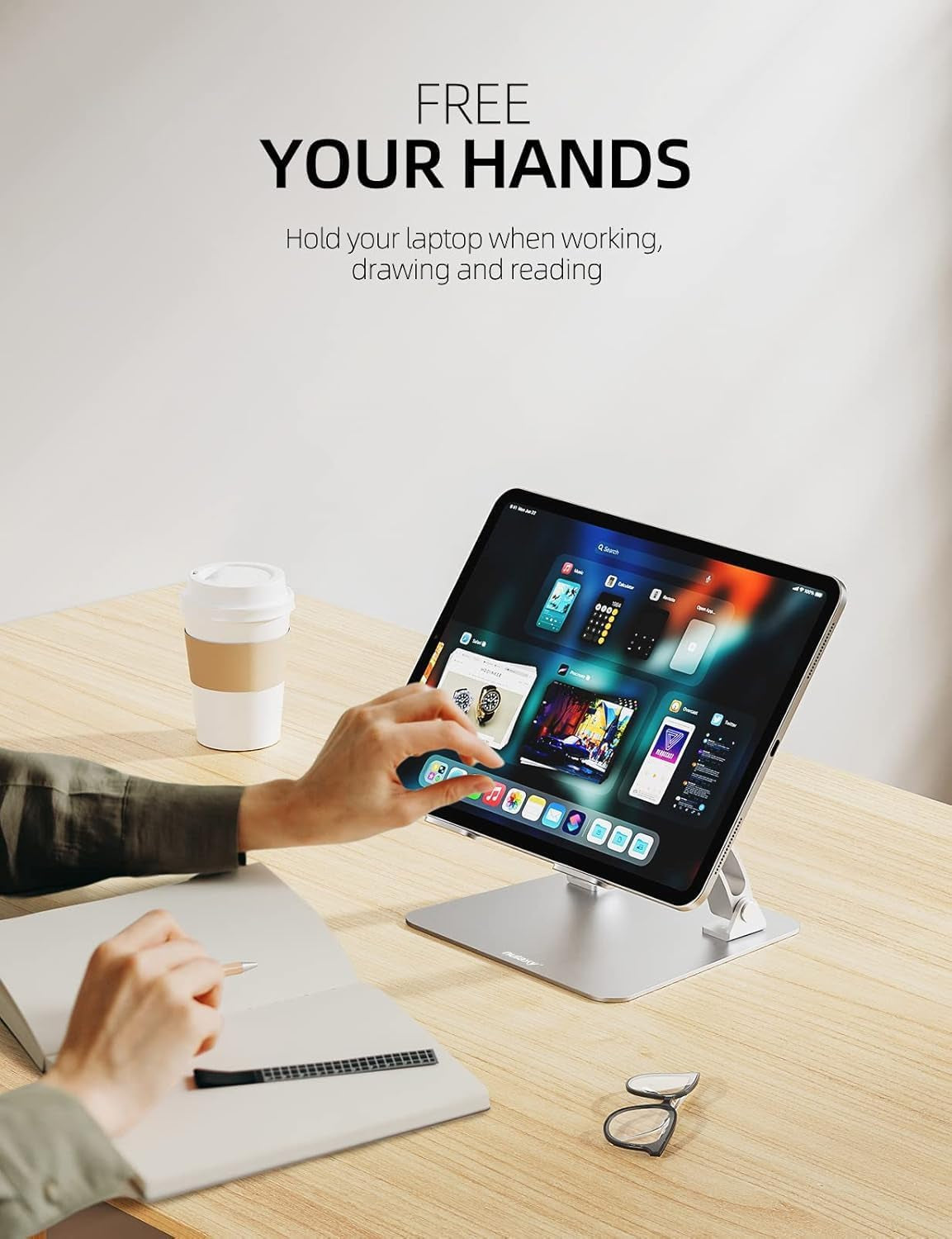 Portrait tablet mounted on the stand being tapped by a hand, with a coffee cup, notebook and glasses on the desk.