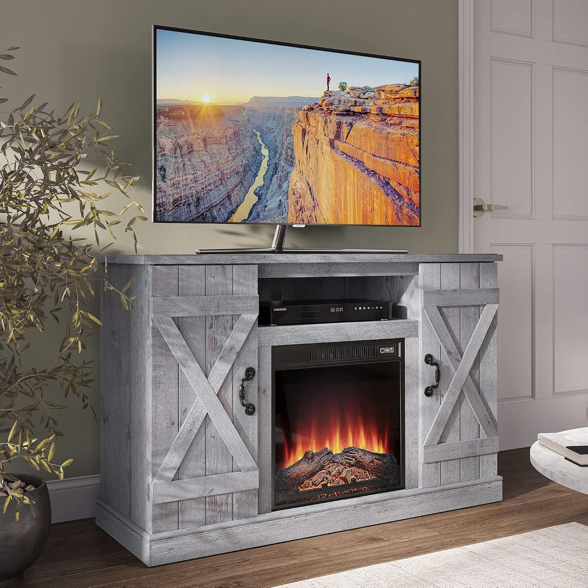 Angled room view of the ash-grey TV stand with lit fireplace, TV on top and a potted plant at left