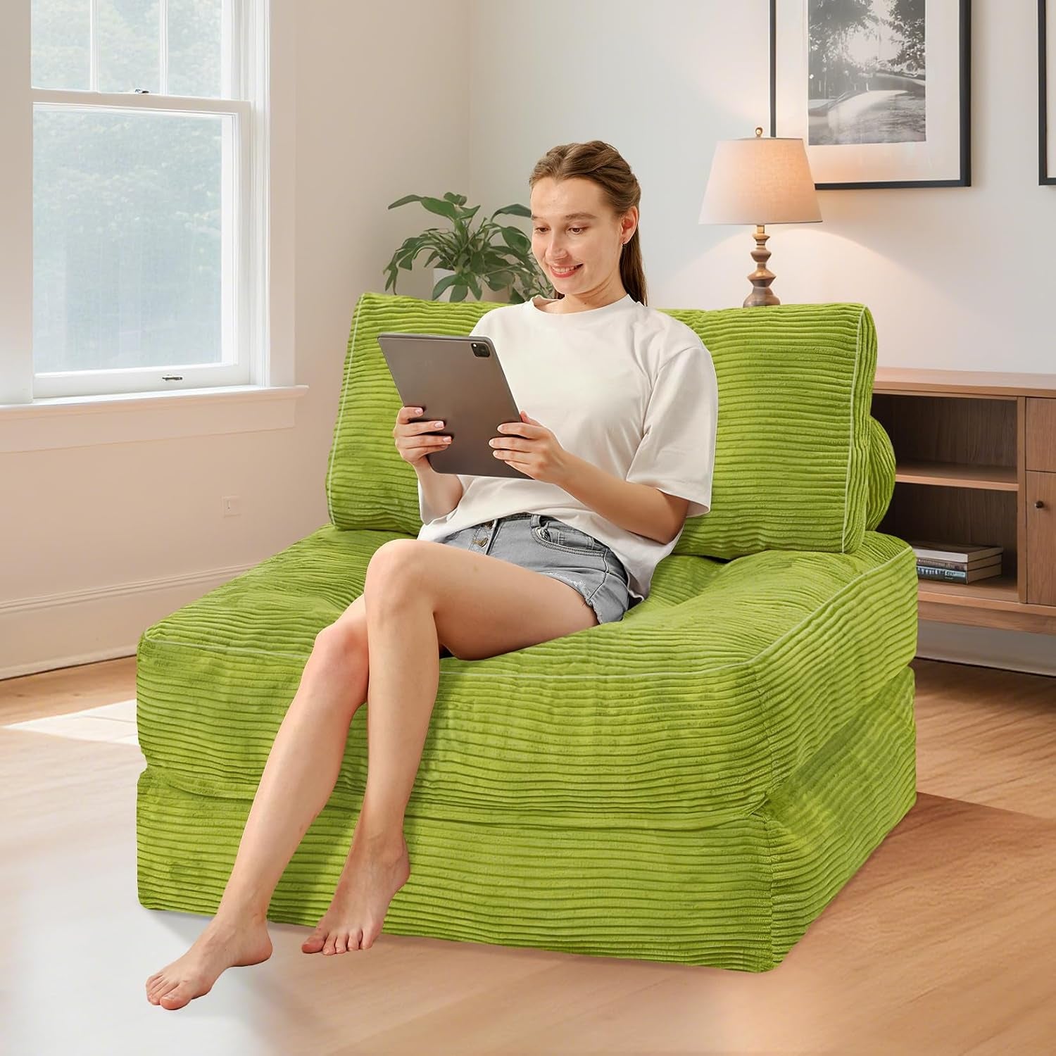Woman seated on green corduroy folding sofa in a living room reading with back pillow