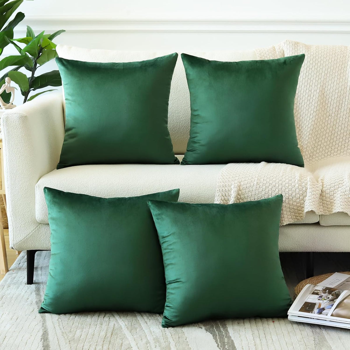 Four square velvet pillow covers in deep green arranged on a light sofa with a knit blanket