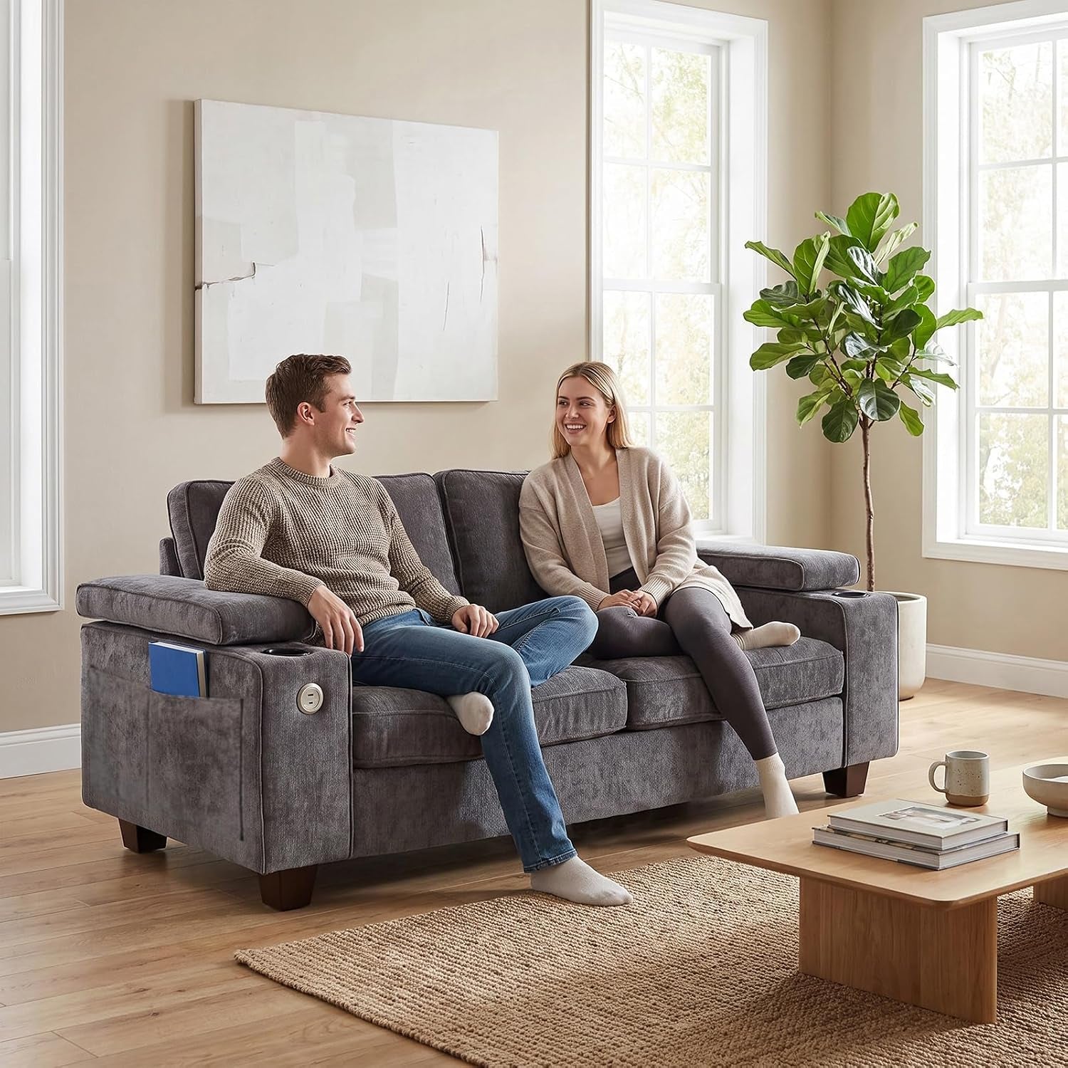Main shot of a dark gray loveseat with two people seated, visible cup holder and side pocket on the armrest.