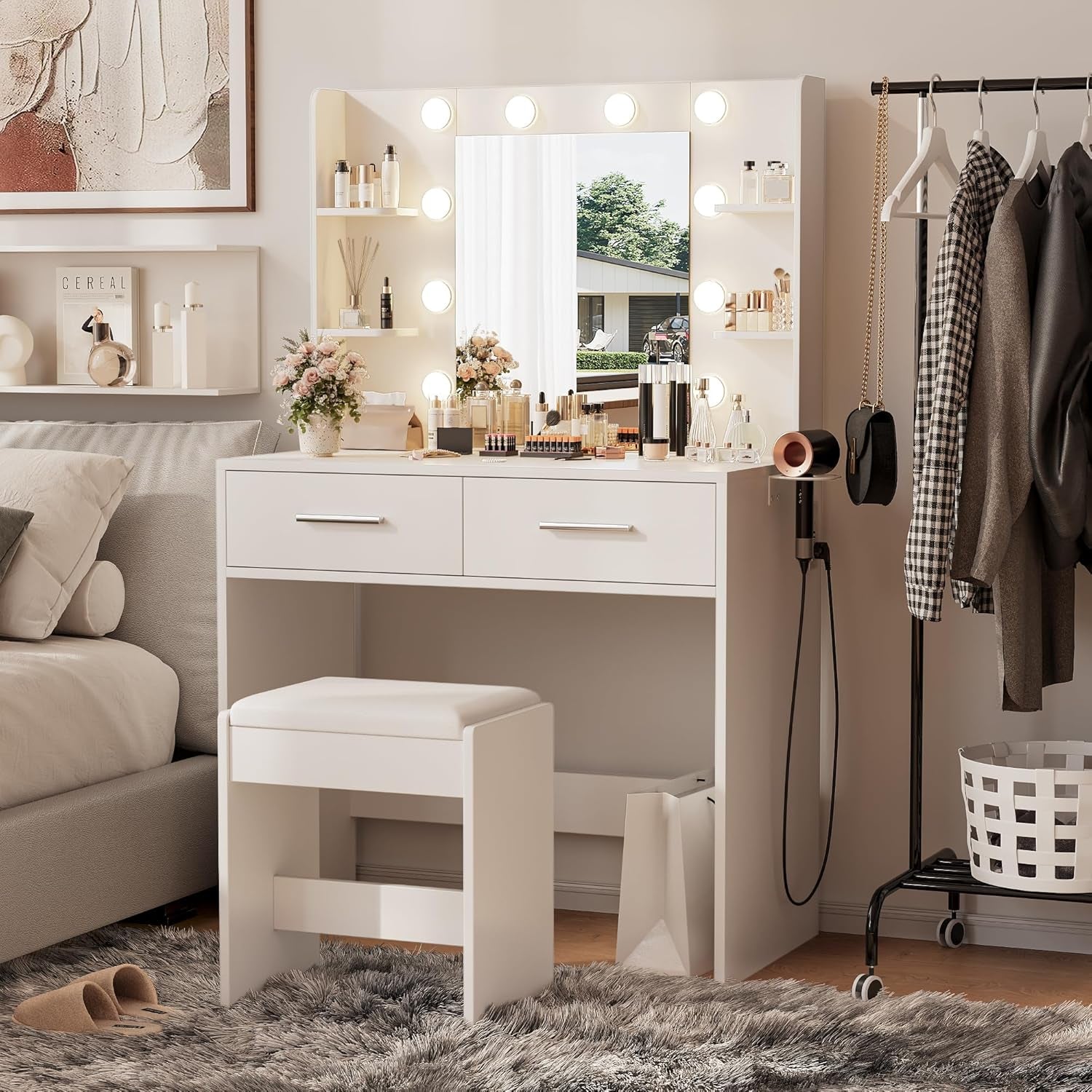 Bedroom scene with illuminated white vanity, bench and nearby clothing rack in a styled interior.