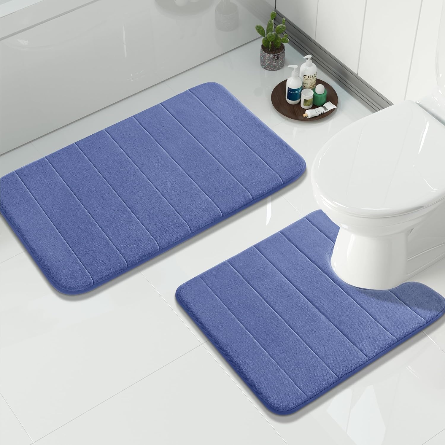 Blue rectangular bath mat and U-shaped toilet contour rug on a glossy tile floor next to toiletries