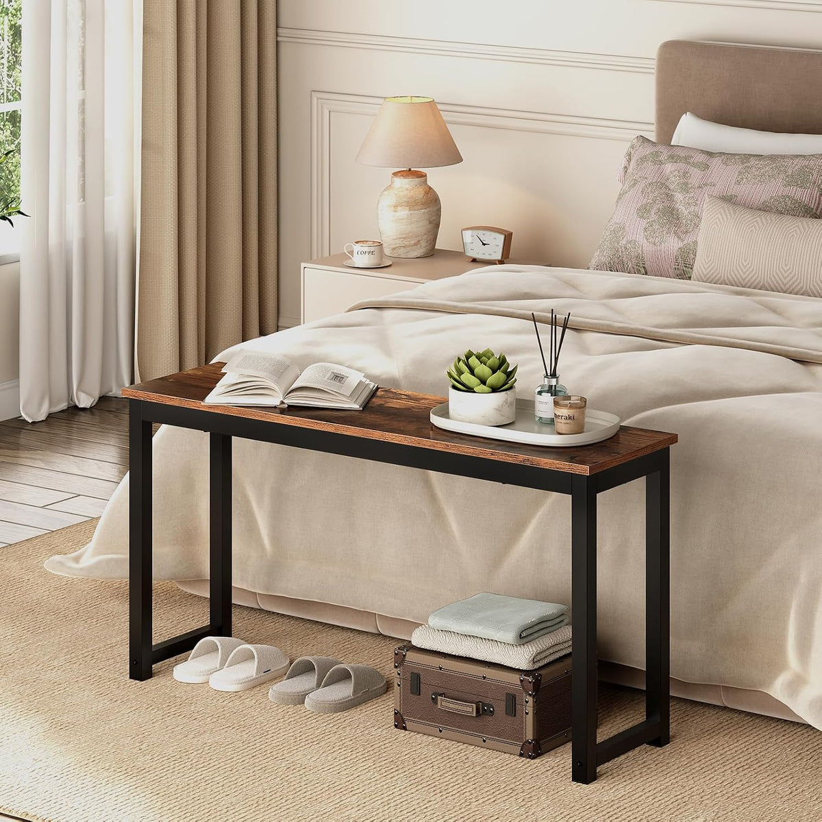 Single bench at the foot of a bed holding a tray and plant, slippers and a trunk tucked underneath.