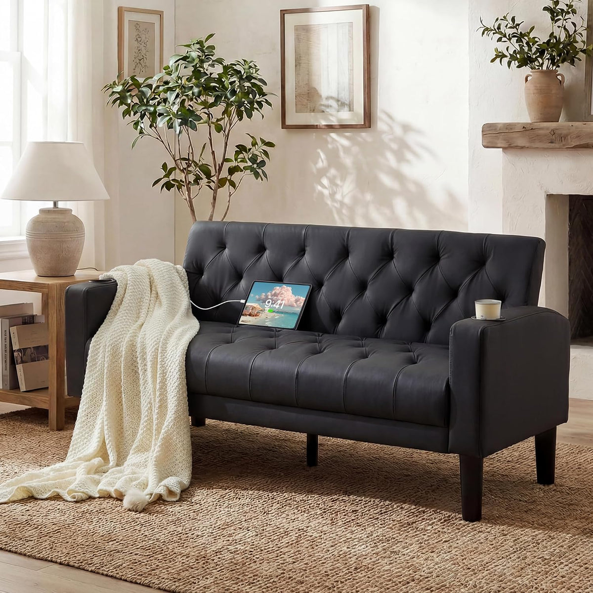 Black tufted loveseat with tablet charging on the seat, cream knit throw draped over the arm and candle on the other arm.