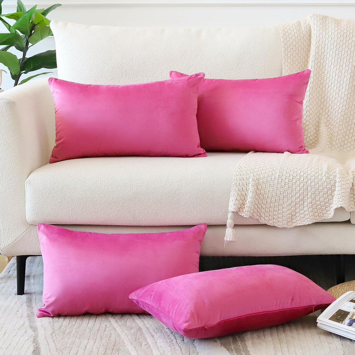 Bright pink rectangular and square pillow covers arranged on a light sofa with a knit throw.