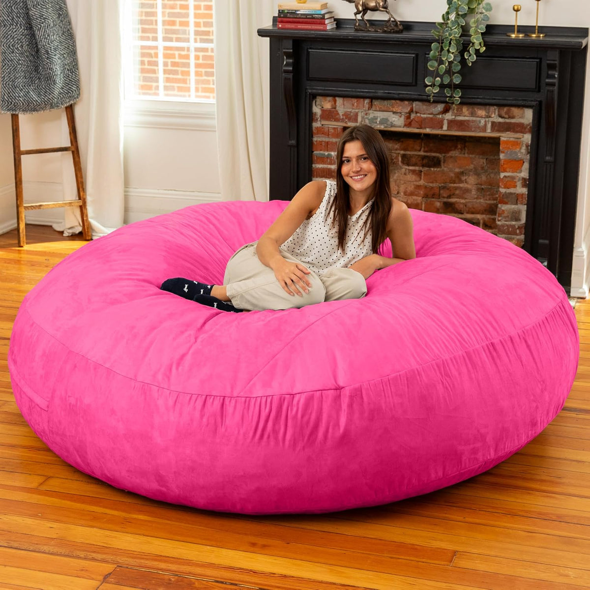 Smiling woman seated in the center of a large bright pink round bean bag in a wood-floored room