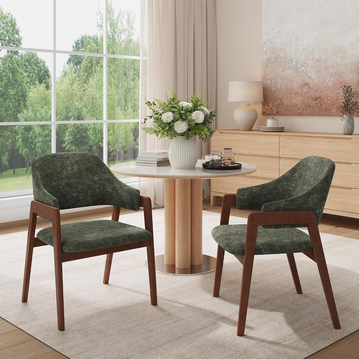 Two forest-green upholstered dining chairs with dark wood frames flanking a small round pedestal table by a large window.