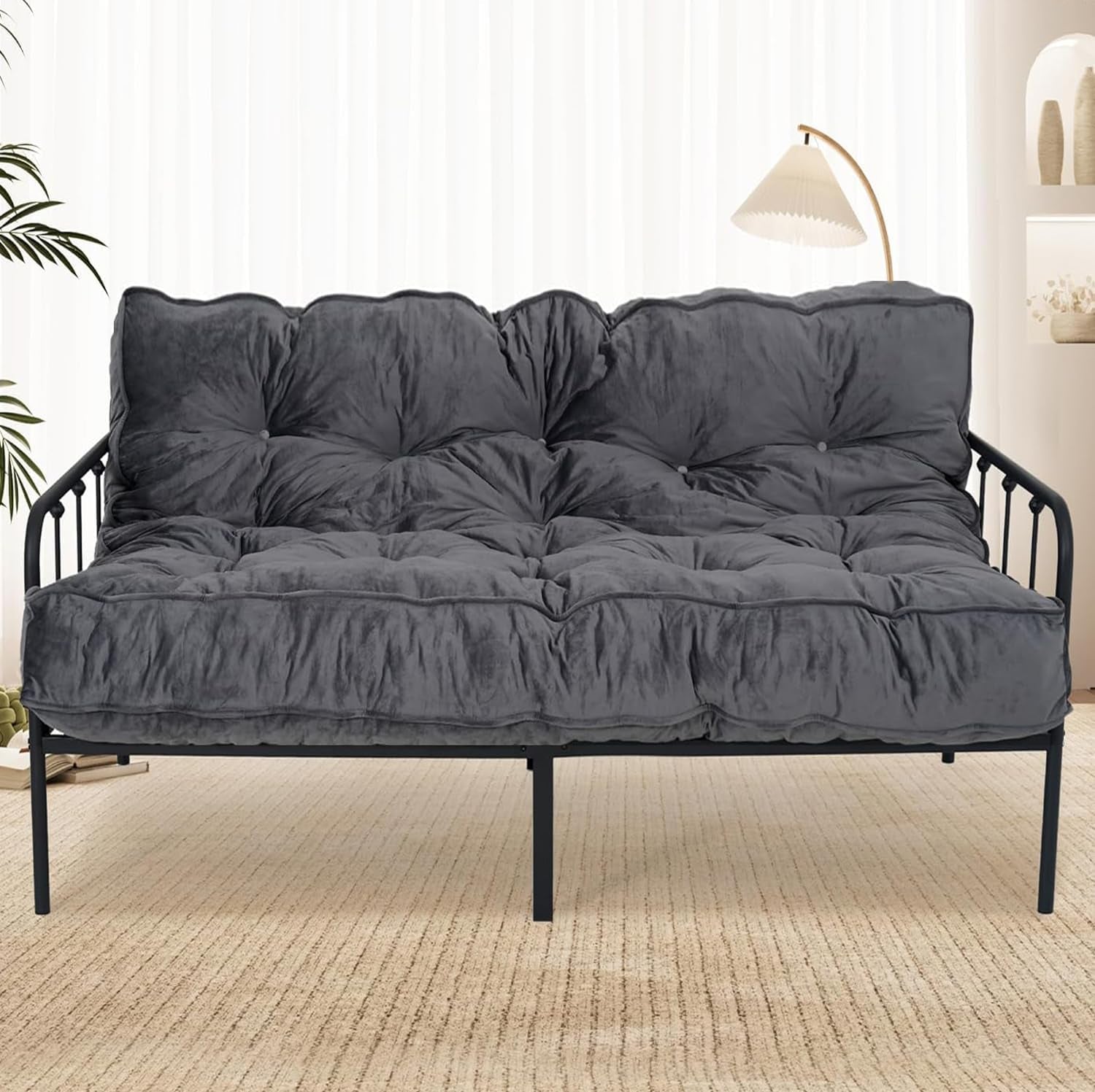 Dark gray tufted futon mattress placed on a black metal sofa frame in a bright room.