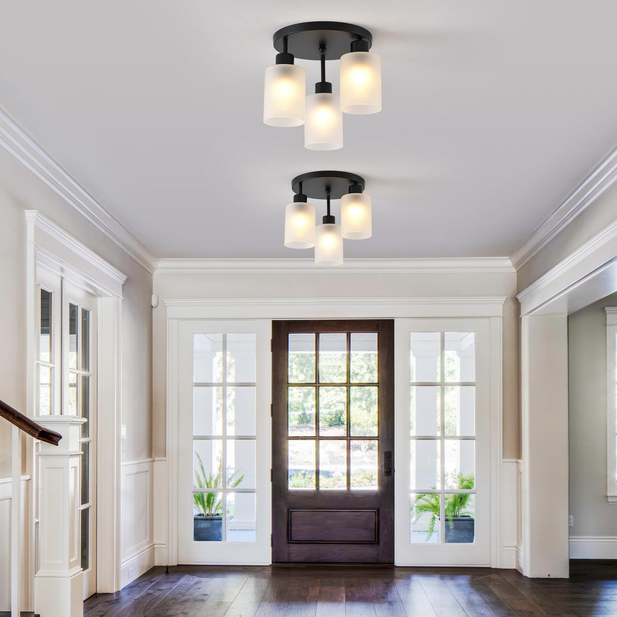Two identical three-light fixtures mounted on the ceiling of a bright foyer with a paneled wood door.