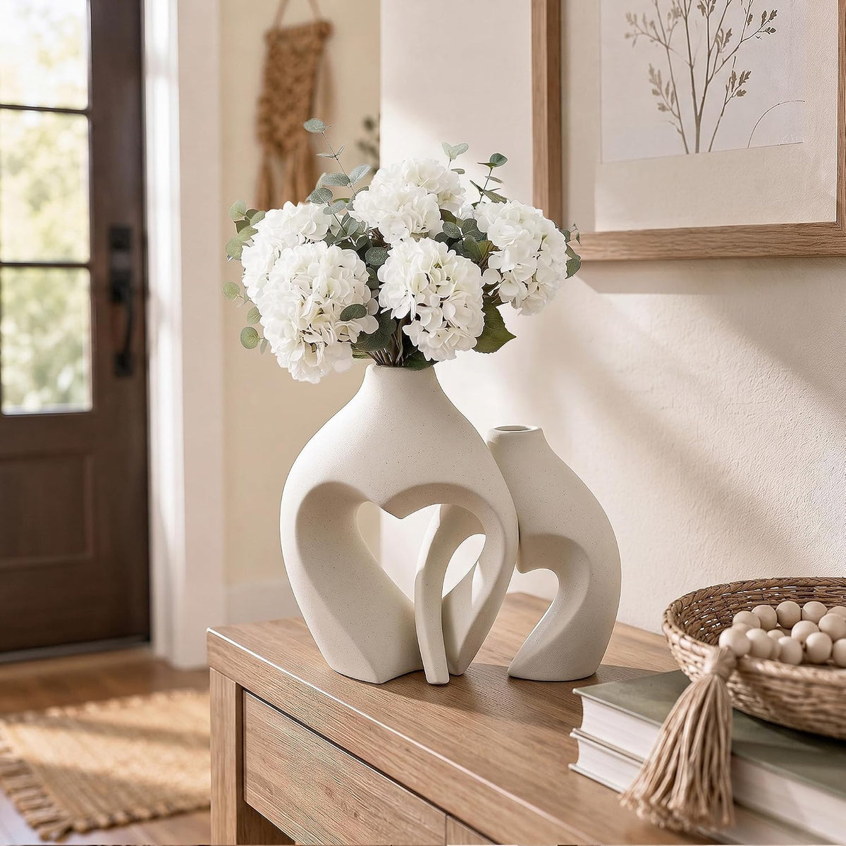 Pair of heart vases on an entryway console by a door, topped with white hydrangea stems
