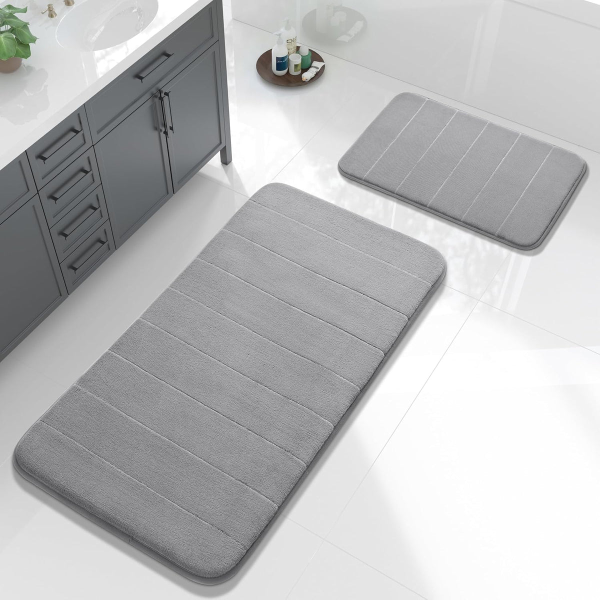 Overhead view of two rectangular gray bath mats placed on a glossy white tiled bathroom floor