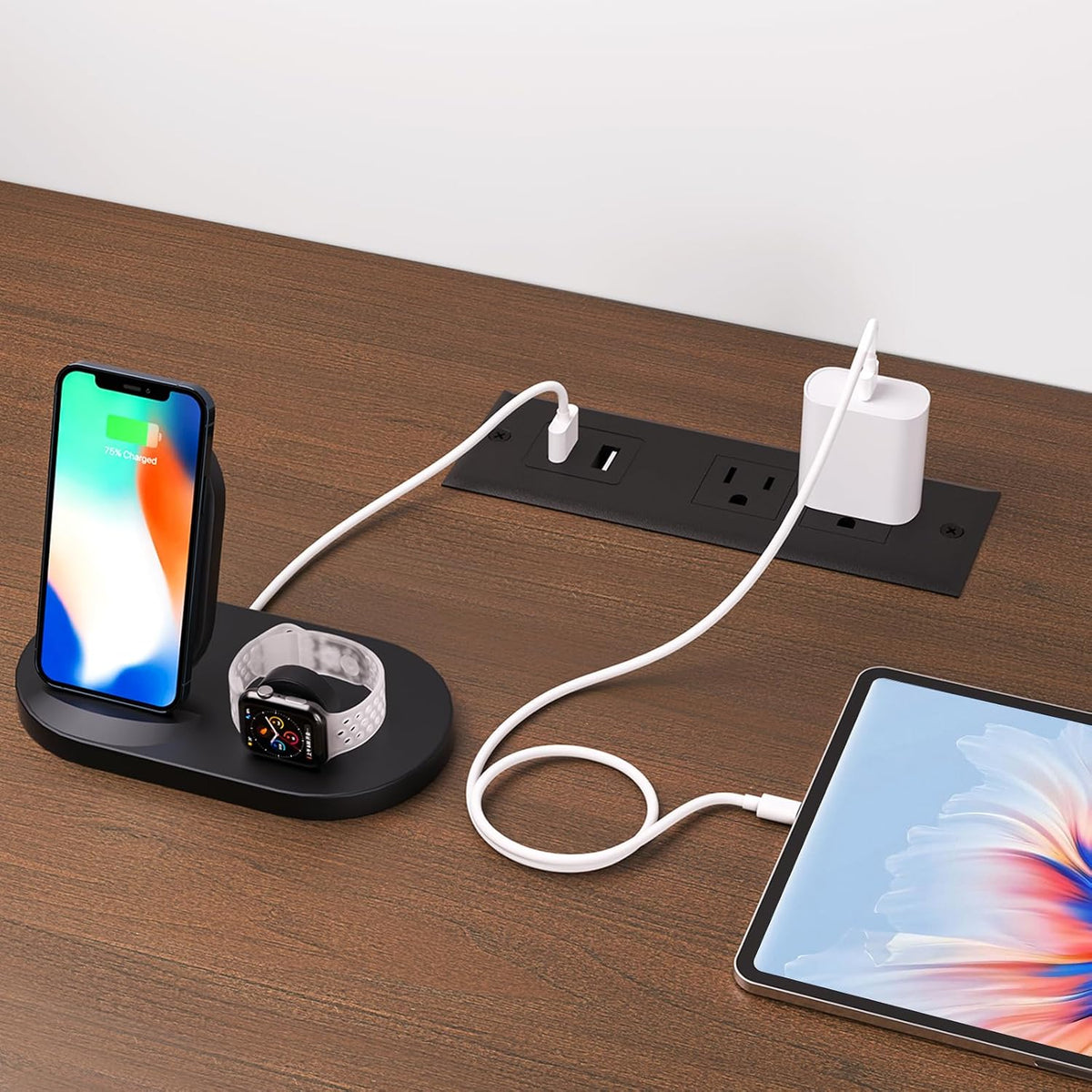 Close-up of the tabletop power outlet inset with a phone, tablet and watch charging on the wood surface.