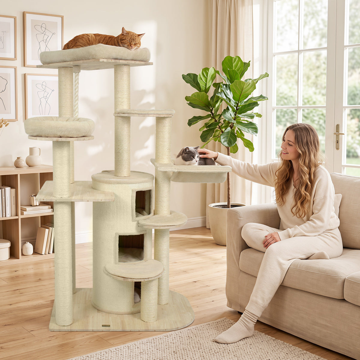A tall beige cat tree beside a sofa, with two cats and a woman reaching toward a cat on a perch.