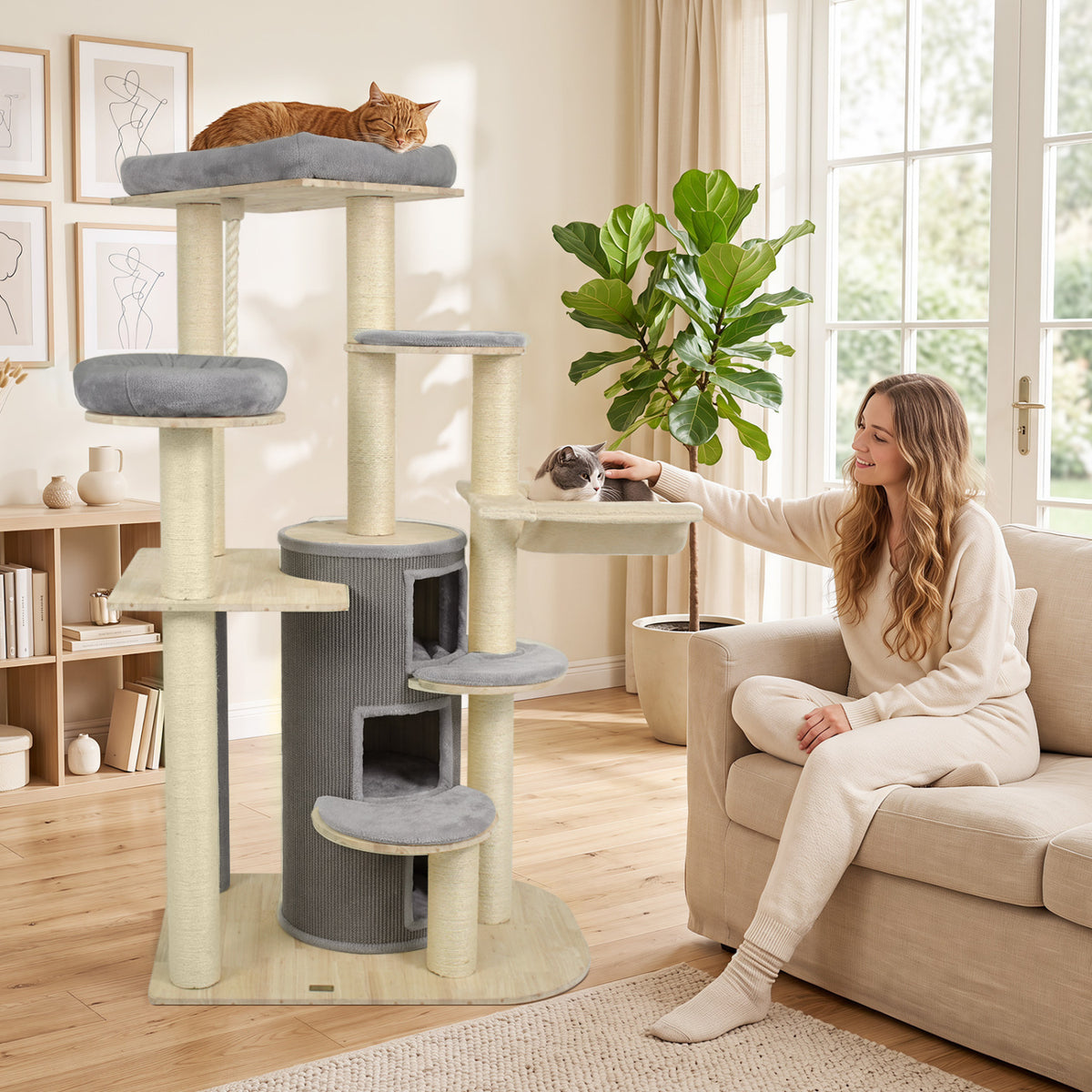 A tall gray and beige cat tree stands beside a sofa as a woman pets a cat on its platform.
