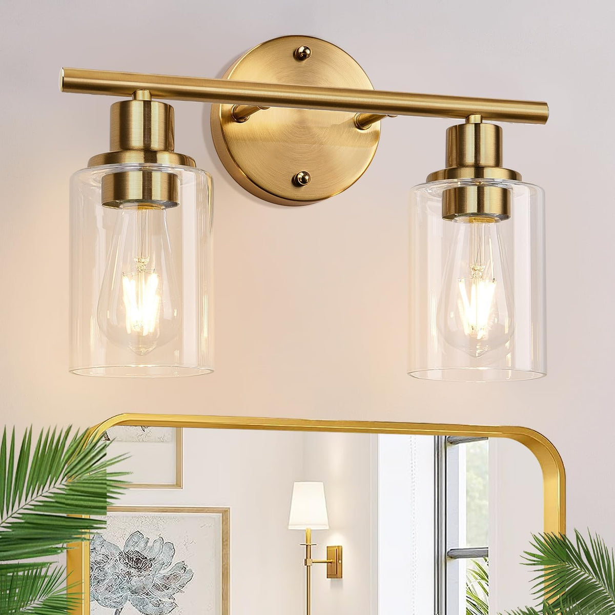 Two gold wall sconces with clear cylindrical glass shades mounted above a mirror.