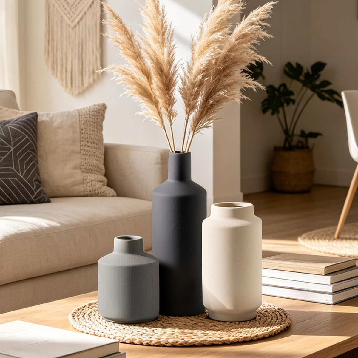 Three matte ceramic vases in charcoal, cream and gray grouped on a woven placemat on a wood table in a living room