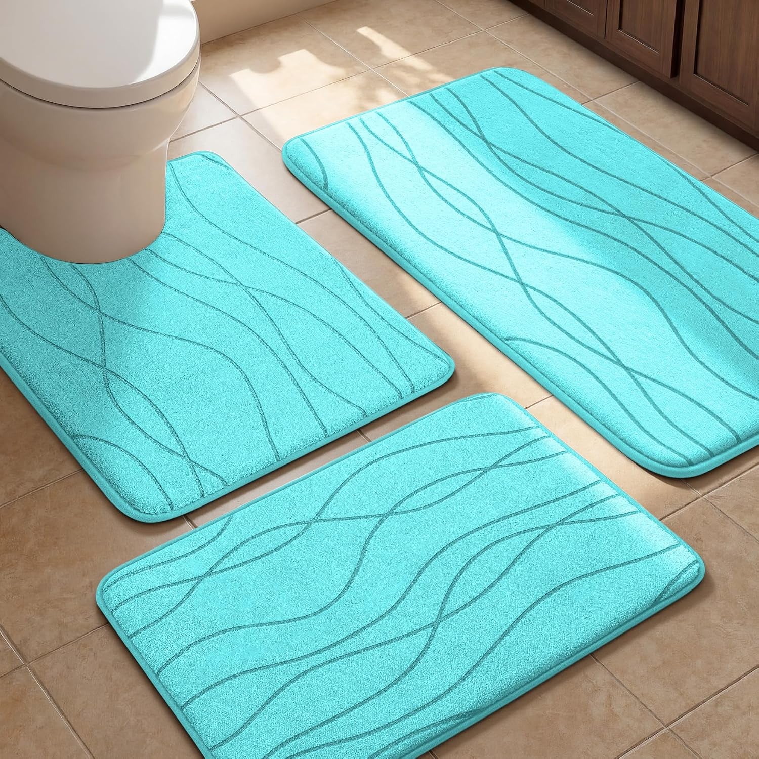 Three aqua bath mats with wavy embossed lines arranged on a tiled bathroom floor around a toilet.