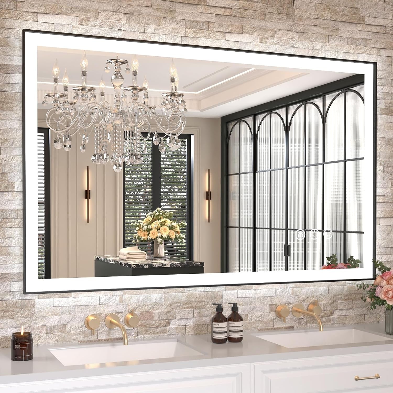 LED rectangular mirror mounted on a stone-tile wall reflecting a crystal chandelier above a double sink vanity.
