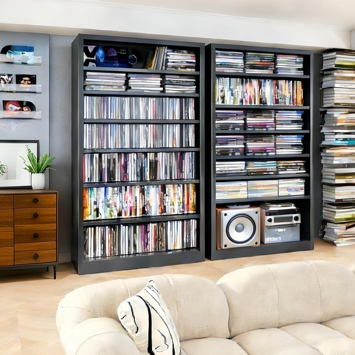 Pair of tall black metal media cabinets filled with stacked CDs and a speaker, sofa visible in the foreground.