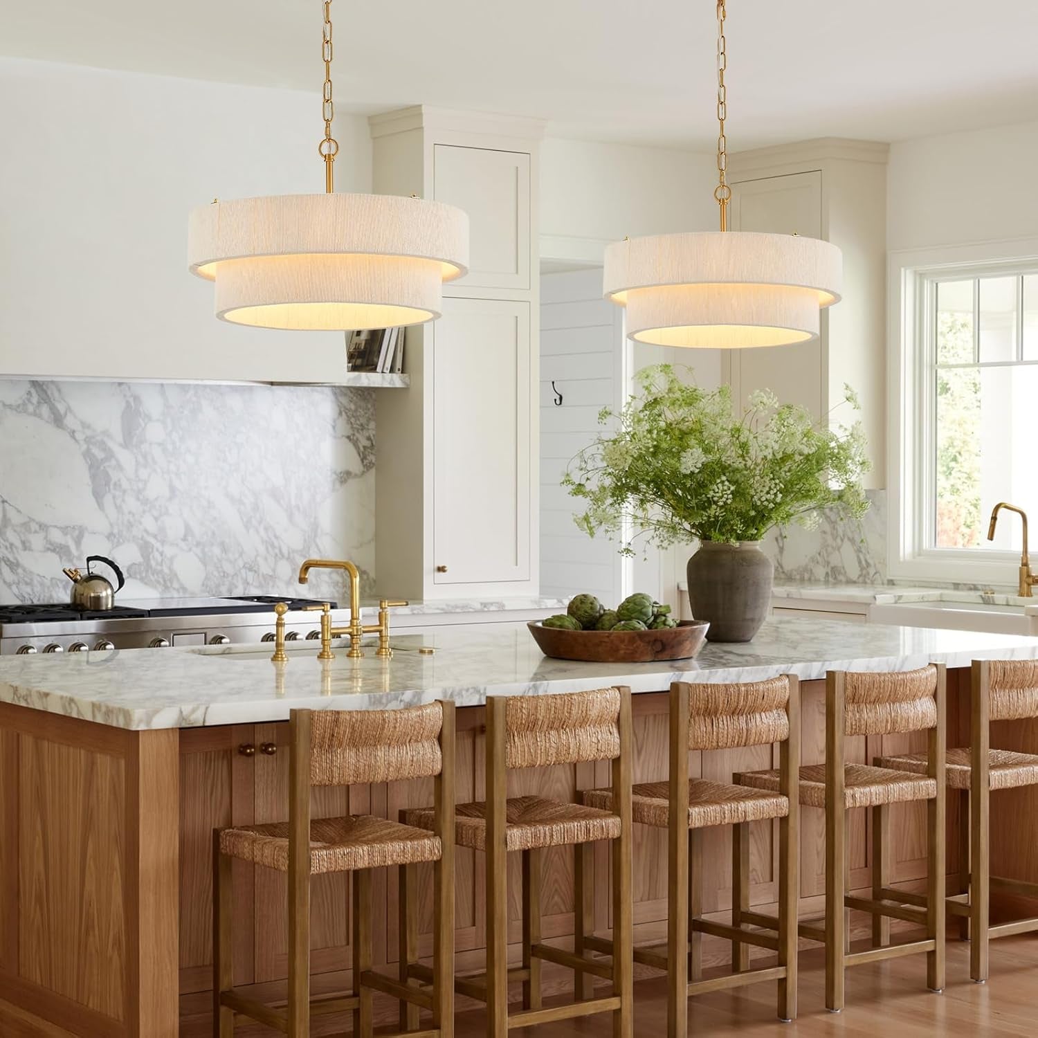 Pair of cream two-ring rattan chandeliers hung above a kitchen island with marble countertop and bar stools
