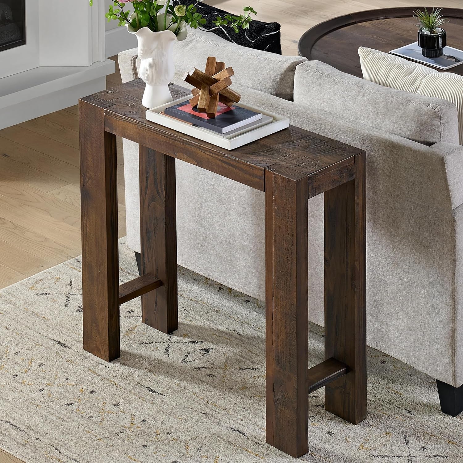 Warm brown pine console table behind a sofa styled with a tray, books and a white sculptural vase.