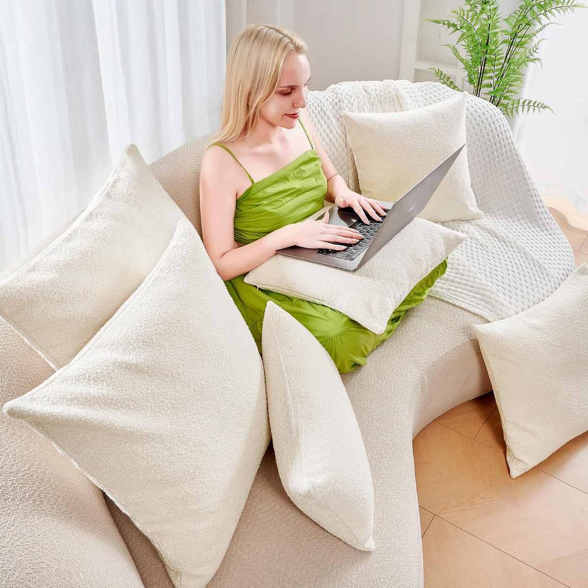 Living room scene with multiple ivory boucle pillow covers on a sofa and a woman using a laptop