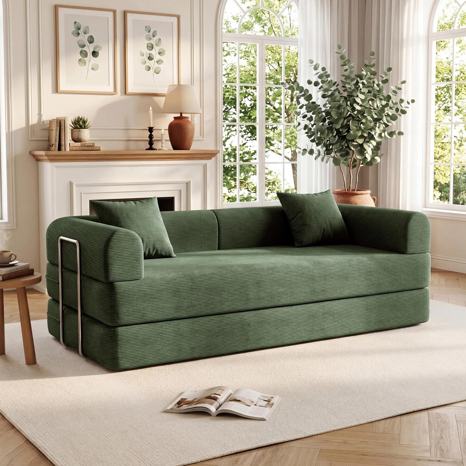 Angled view of a green corduroy sofa bed with metal side frame, two pillows, and large arched windows behind it.