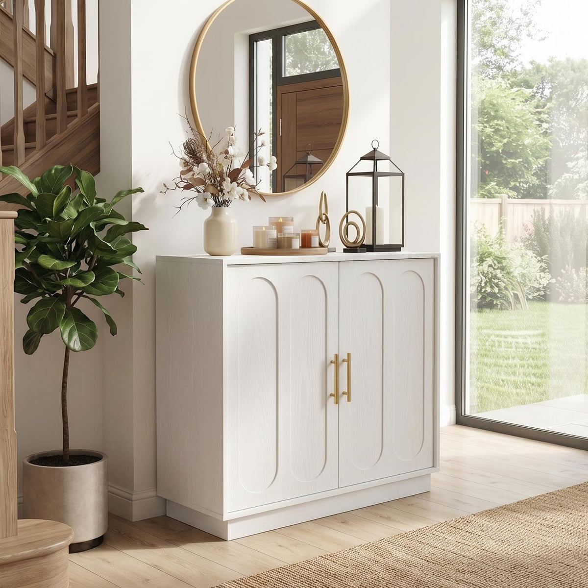 White fluted storage cabinet under a round gold mirror, styled with a vase, candles and lantern.