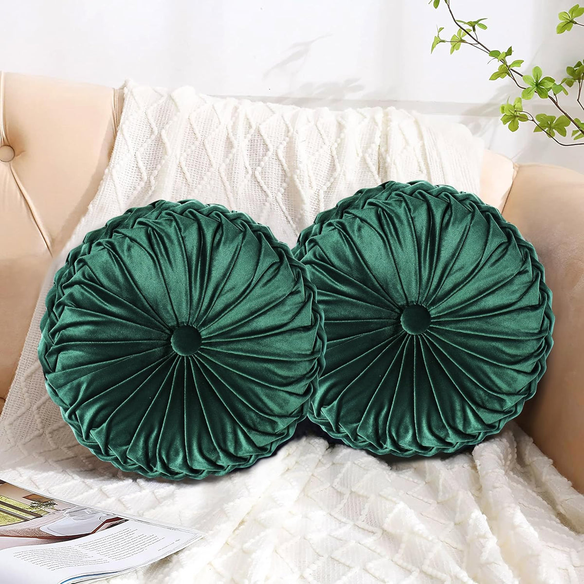 Two round ruched velvet throw pillows in deep emerald green on a cream knit throw and sofa.